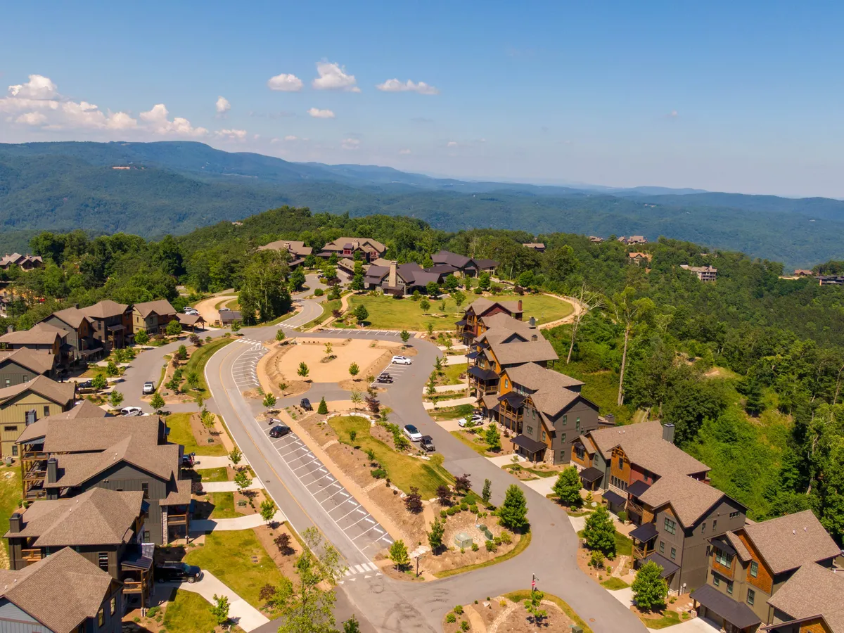 A wide exterior shot capturing residential houses nestled along curved roads, set against a backdrop of rolling, mountainous landscape. The scene exudes a welcoming, community-centric vibe and hints at a sense of growth and expansion within the area.