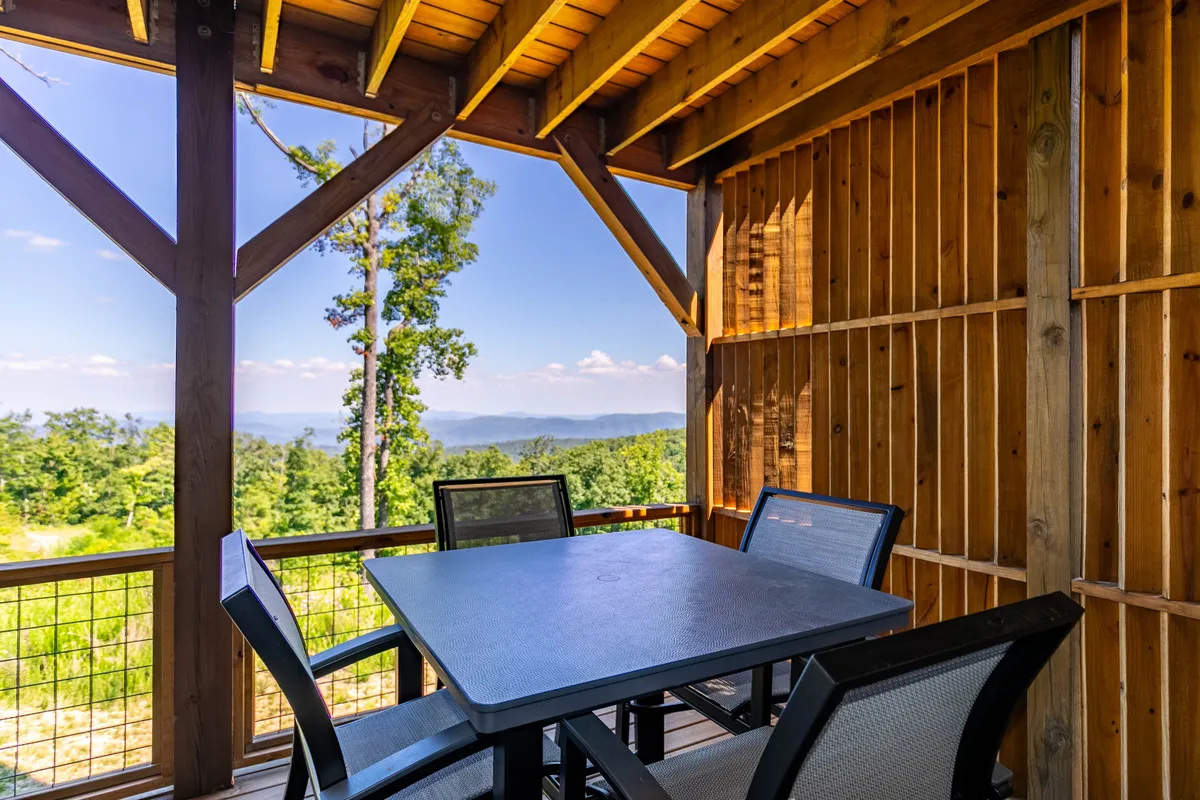 An inviting outdoor dining area set on a wooden deck, positioned to take full advantage of sweeping mountain views. The setting suggests possibilities for al fresco meetings, meals, or laptop sessions in a peaceful, natural environment. The structure’s openness connects the living space with the outdoors.