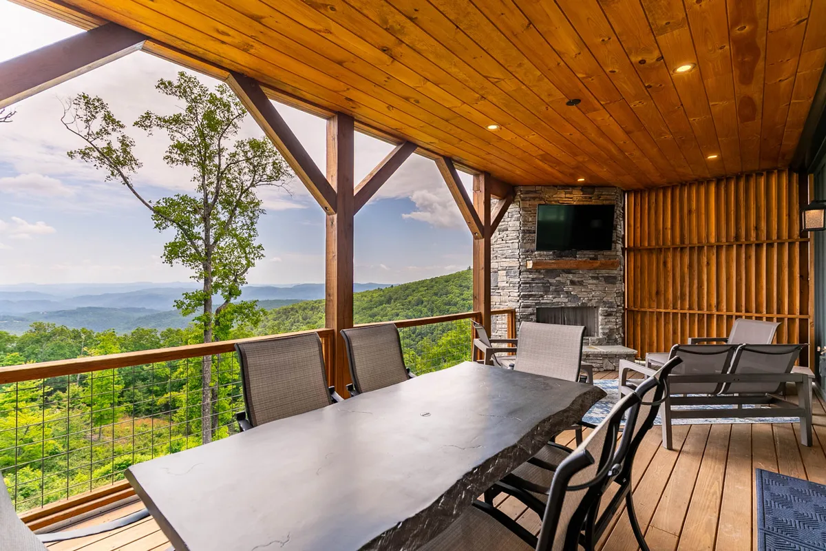 A spacious outdoor dining area features a large table and a stone fireplace, all set against a scenic mountain backdrop. This space is designed for group dining, celebrations, and relaxing by the fire, reinforcing the community's social vibe.