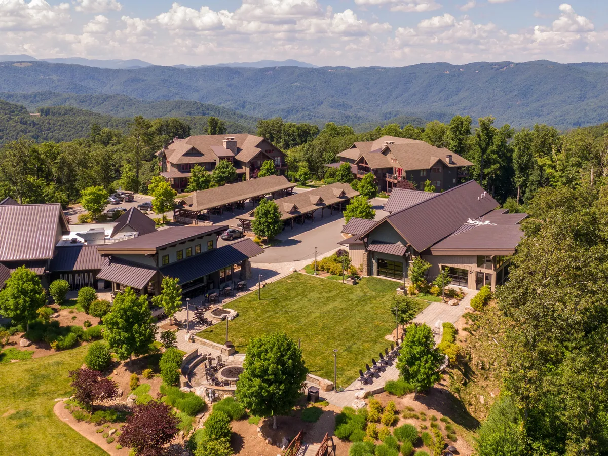 A wide green lawn framed by distant mountains, multiple community buildings, and inviting outdoor seating areas. The setting is vibrant and tranquil, ideal for group activities, family gatherings, or simply enjoying the natural beauty.