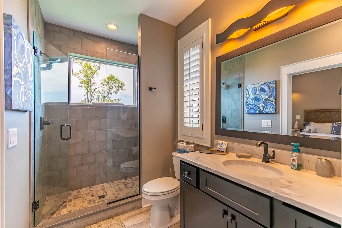 A modern, well-lit bathroom featuring a glass shower enclosure, elegant vanity, large mirror, and tasteful wall art. The space feels both refreshing and tranquil, ideal for unwinding after a day of adventure.