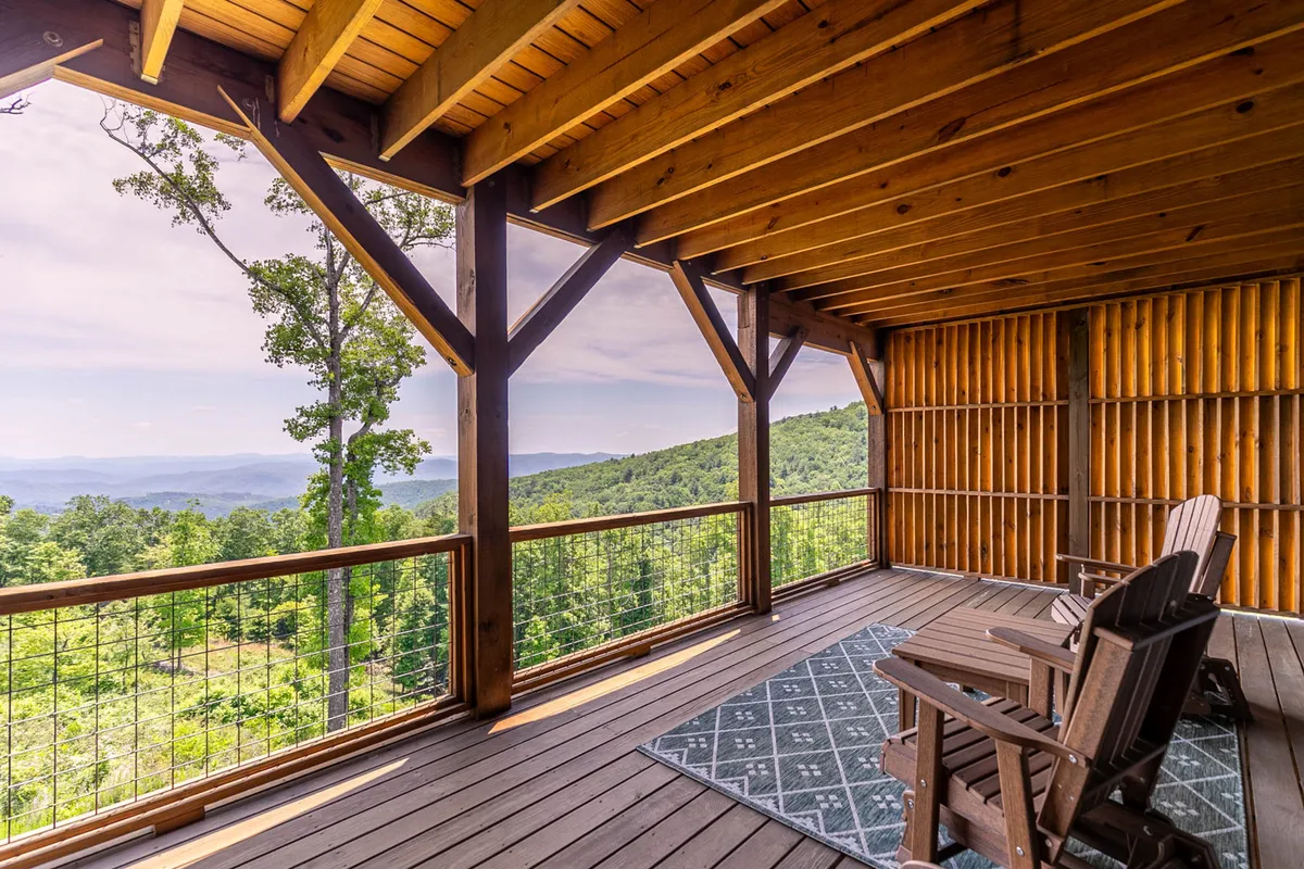 Two wooden rocking chairs placed on a deck overlooking an expansive mountain vista, with textured wooden beams and a cozy, inviting atmosphere. The setting is perfect for quiet reflection, group photos, or stargazing at night.