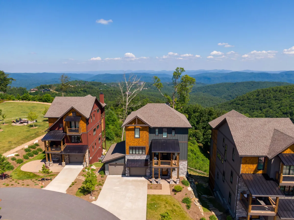 This image features three modern houses nestled in a lush green landscape, with a distant mountain range as the backdrop. The setting is open and inviting, emphasizing expansive natural surroundings ideal for outdoor exploration.