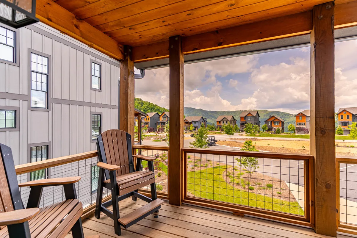 A serene exterior scene featuring classic rocking chairs on a deck, overlooking distant mountains and neighboring cabins. The peaceful ambiance suggests moments of contemplation, downtime, or casual work while immersed in the natural surroundings.