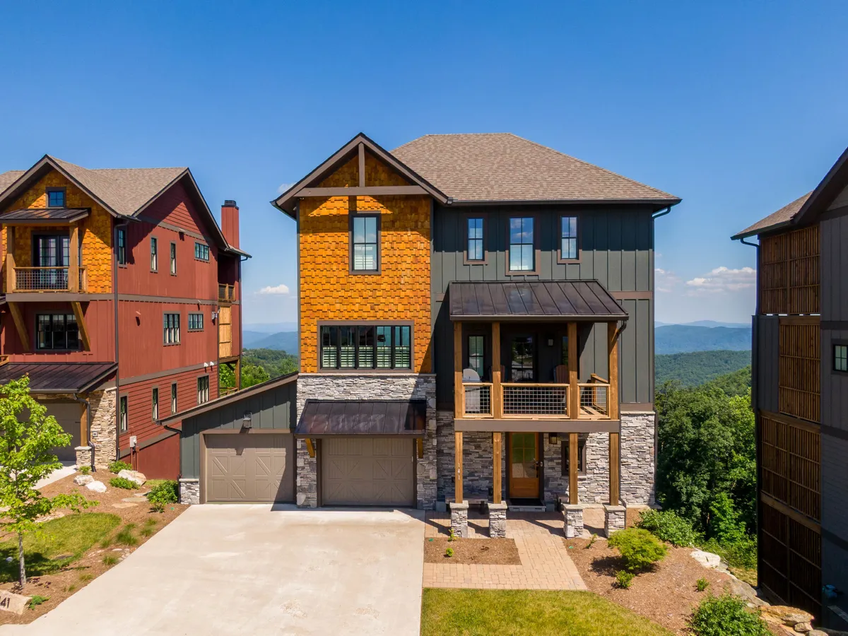 The image showcases the exterior of a luxurious single-family home crafted from wood and stone, featuring a spacious porch with railings that overlooks breathtaking long-range mountain views. The inviting porch hints at gatherings and relaxation, while the backdrop of the Blue Ridge Mountains sets a tranquil, picturesque scene.