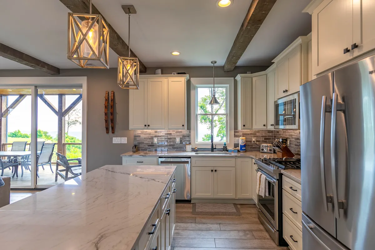 An open, modern kitchen with a large island, sleek appliances, hanging light fixtures, and expansive windows allowing natural light to flood the space. The setting suggests lively meal prep, entertaining guests, and relaxed family time.