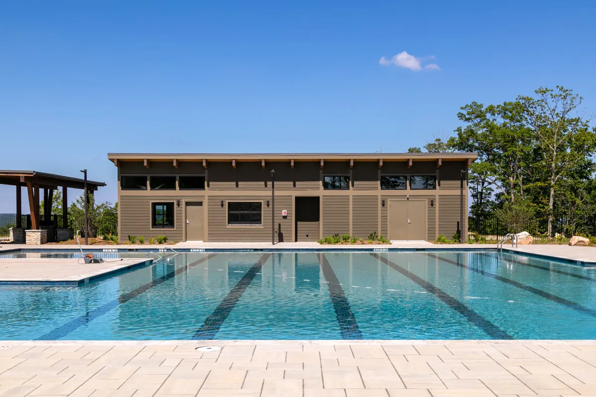 The community swimming pool is surrounded by trees and features a nearby community center building. The inviting poolside area suggests relaxation and opportunities for social interaction, with the environment emphasizing seasonal amenities.