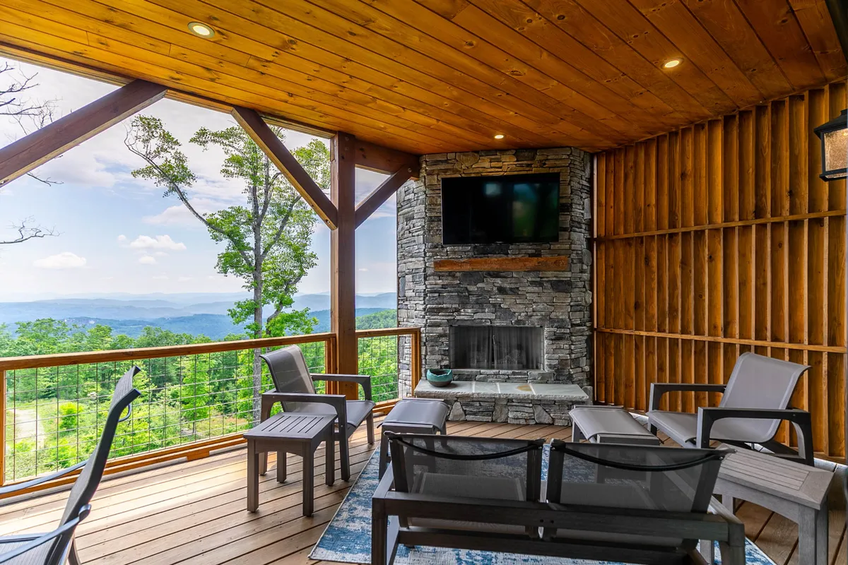 An outdoor living area with a stone fireplace, comfortable seating, and spectacular views of the mountains beyond. Wooden beams overhead add rustic charm, creating a cozy spot for relaxing or socializing outdoors.