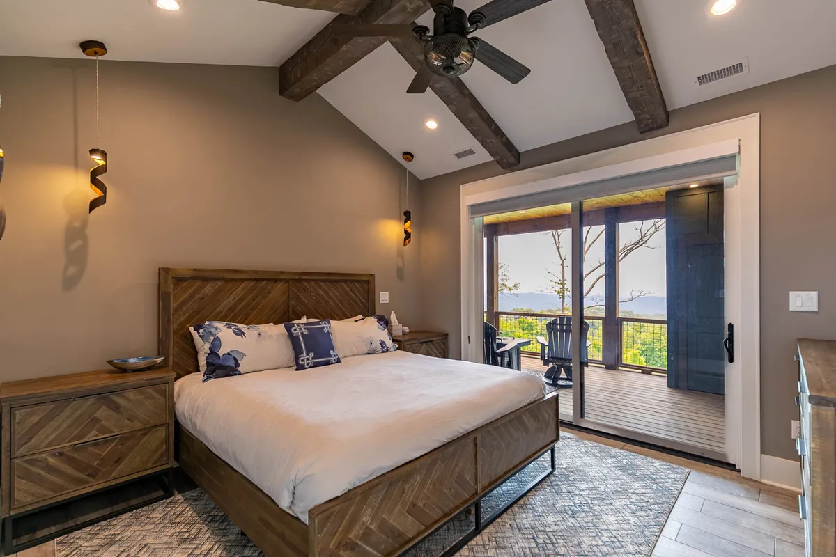 A serene bedroom with a wooden bed frame, decorative throw pillows, and a large window offering a view of the outdoors. The room features calming, neutral tones, luxurious linens, and tranquil decor, all designed to evoke a restful atmosphere.